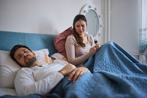 Thoughtful woman sitting on bed and crying while her husband sleeping